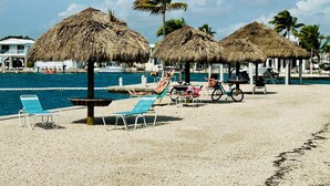 Un complexe hôtelier en bord de mer, doté de parasols en chaume, de chaises longues et d’une piscine.