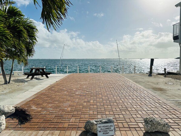 A paved walkway leading to a beach with a picnic table and a sign prohibiting vehicles beyond a certain point. - 219 Oceanfront RV Lot 59' Seawall (Cudjoe Key)