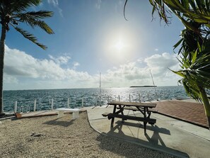 A beachside picnic area with a concrete bench and a wooden picnic table, overlooking the sea. - 219 Oceanfront RV Lot 59' Seawall (Cudjoe Key)
