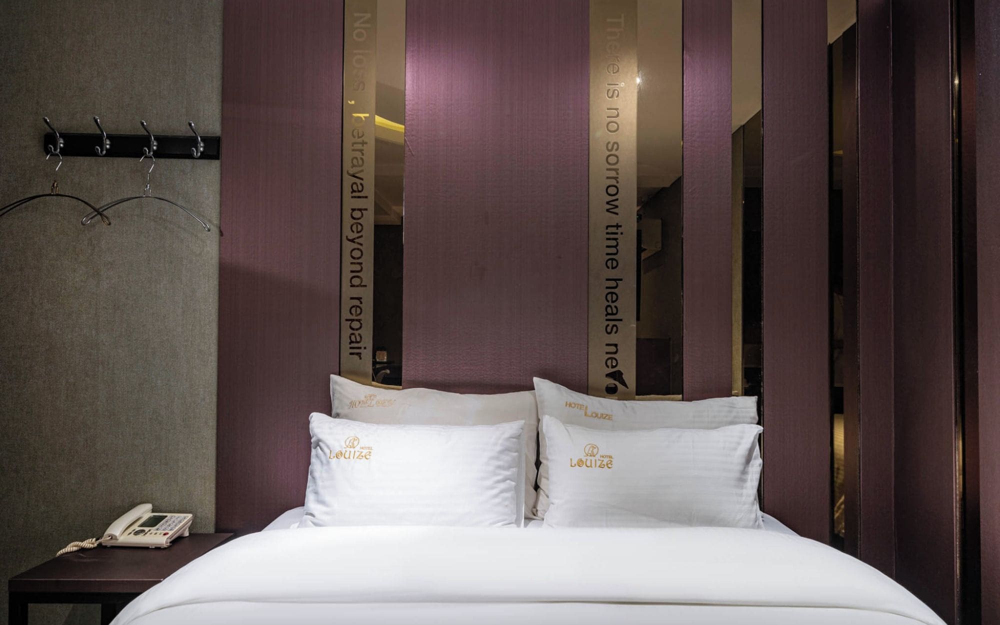 Una habitación de hotel con una cama, almohadas, un teléfono en la mesita de noche y una pared decorada con paneles verticales.