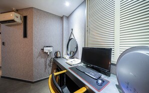 A modern hotel room with a desk, computer, and air conditioning unit.