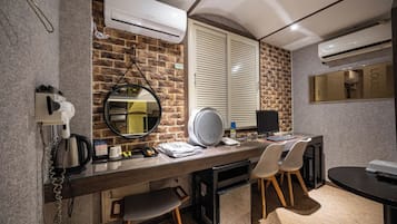Habitación de hotel moderna con pared de ladrillo, espejo redondo, escritorio con computadora y secador de pelo.