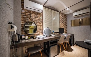 A modern hotel room with a brick wall, a round mirror, a desk with a computer, and a hairdryer. - Hotel Louize (Seoul)