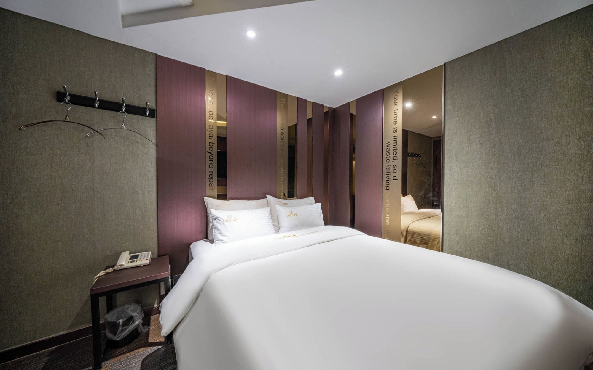 Ein Hotelzimmer mit einem großen Bett, einem Nachttisch mit Telefon und einem Spiegel an der Wand.