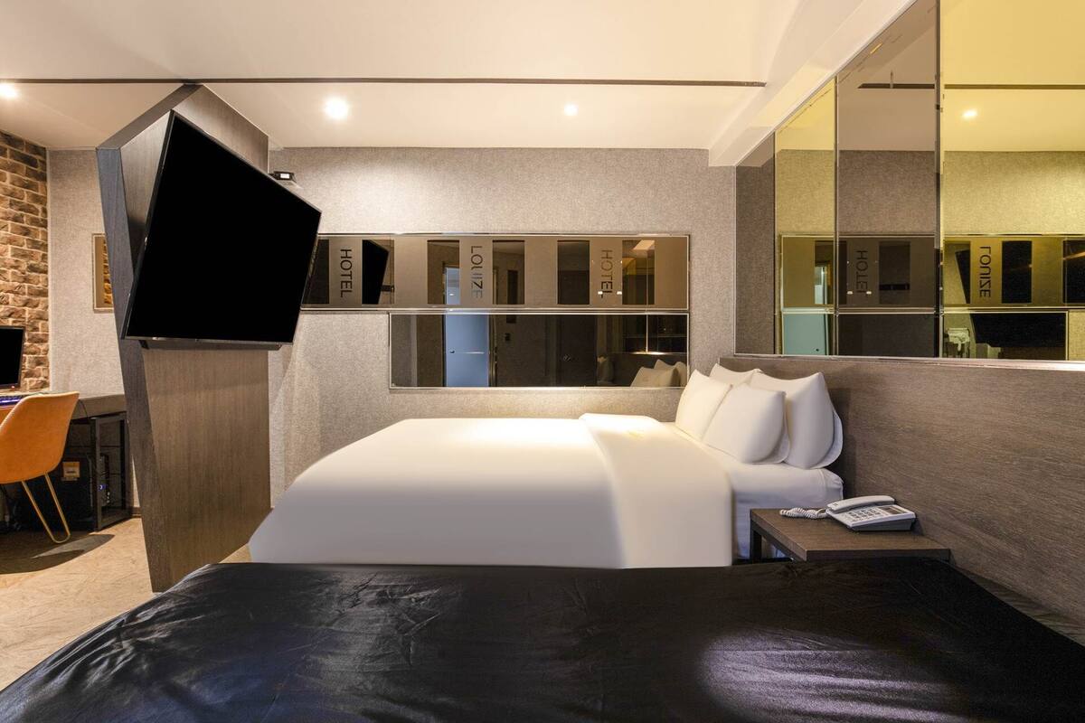 A modern hotel room with a large bed, a desk with a computer, and a TV mounted on the wall.