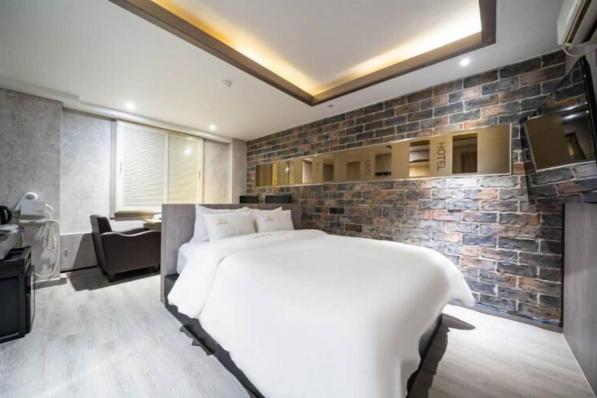 A hotel room with a large bed, a desk, a chair, and a stone wall.