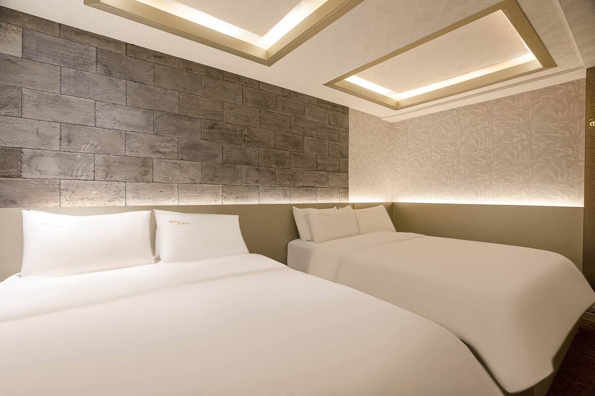 A hotel room with a brick accent wall, two beds with white bedding, and recessed lighting.