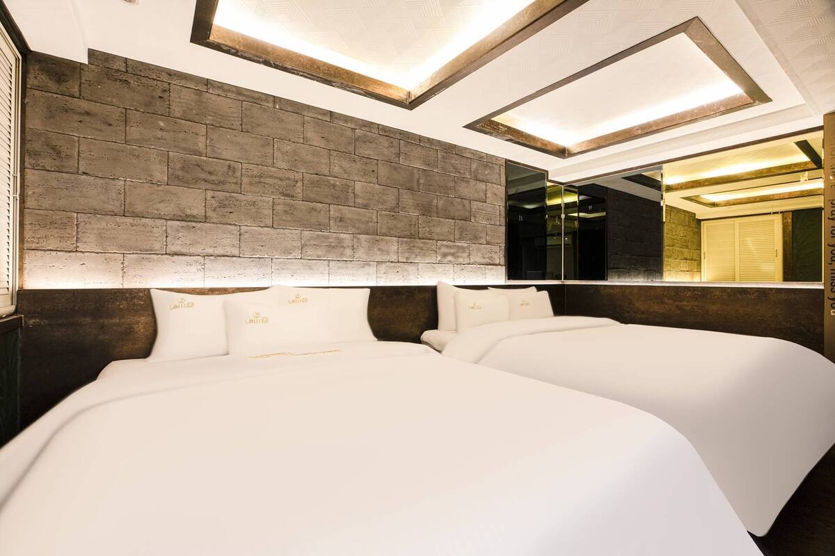 A hotel room with two beds, a brick accent wall, and a large mirror reflecting the room.