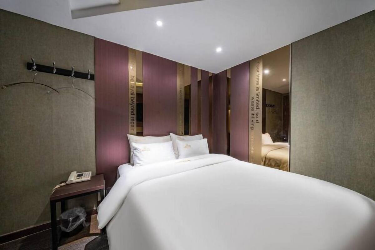 A hotel room with a large bed, a bedside table with a phone, and a mirror on the wall.