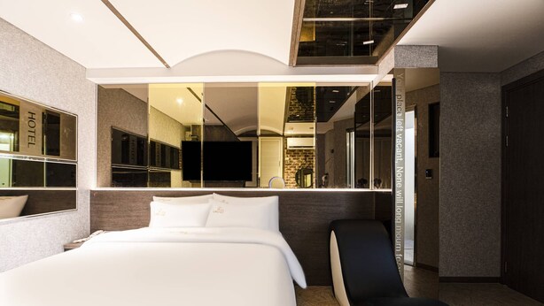 A modern hotel room with a large bed, a sitting area, and a mirror reflecting the room. - Hotel Louize (Seoul)