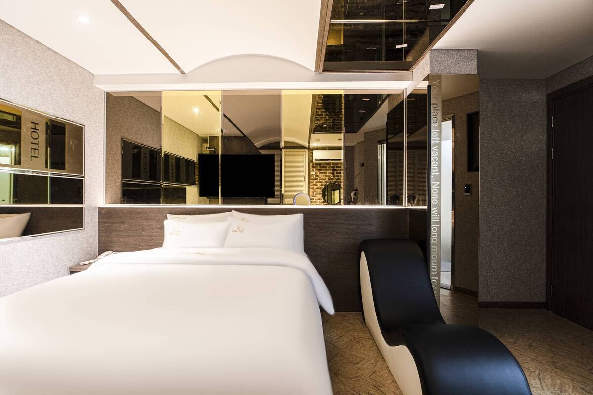 A modern hotel room with a large bed, a sitting area, and a mirror reflecting the room.