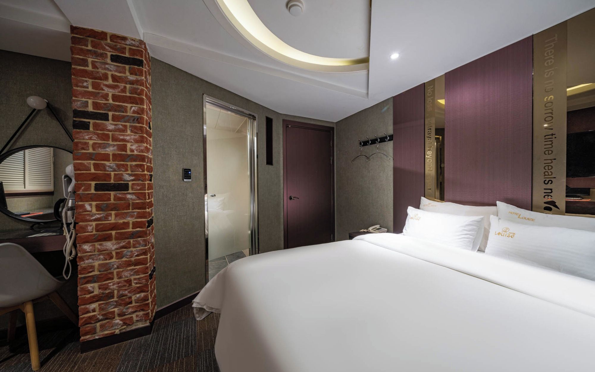 Habitación de hotel con una cama, un muro de ladrillo decorativo, un espejo, un teléfono y un cartel con el nombre del hotel.