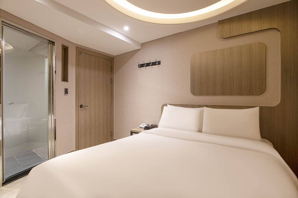 A hotel room with a large bed, a wooden headboard, a bedside table with a phone, and a coat hook on the wall.
