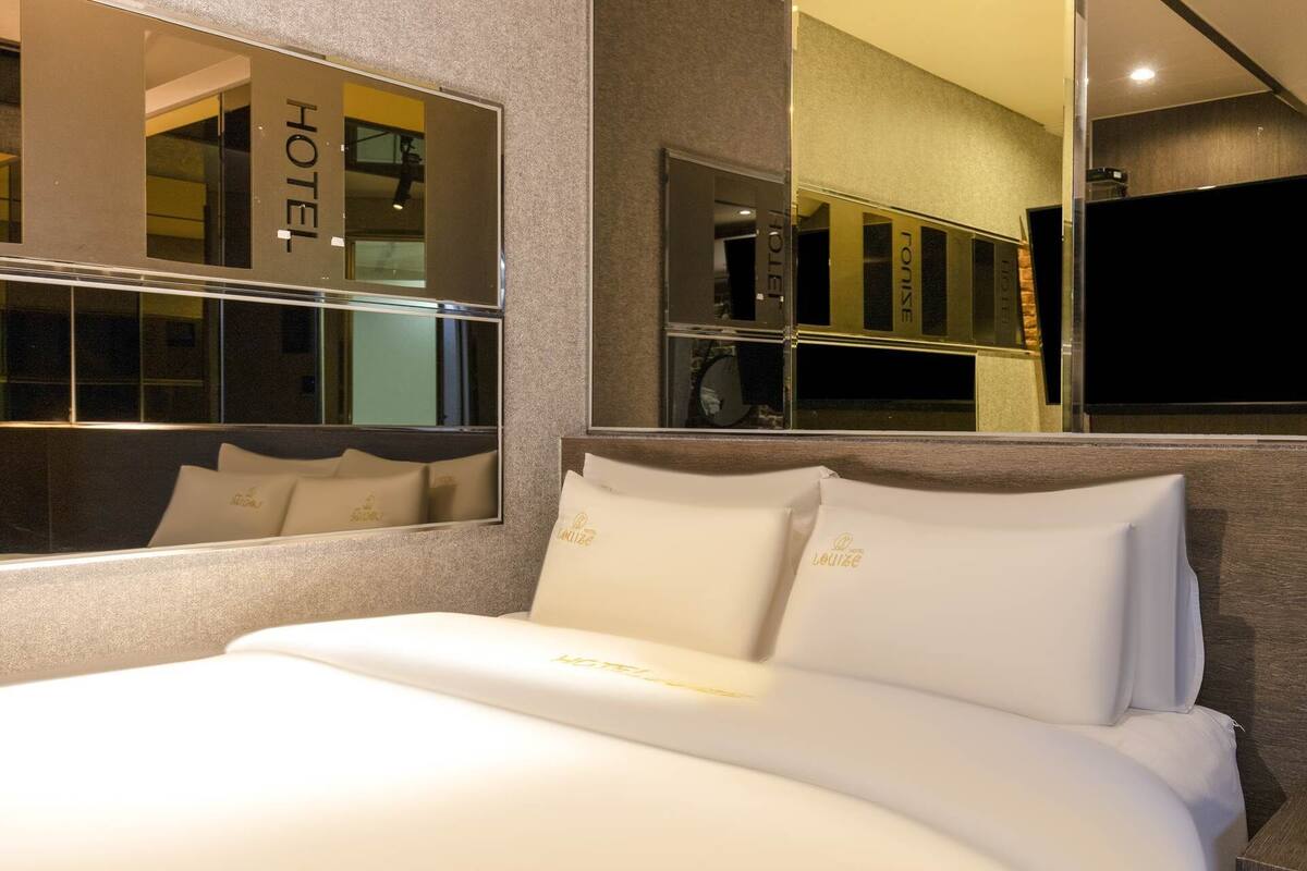 A hotel room with a large bed, a mirror reflecting the room, and a sign reading "HOTEL" on the wall.