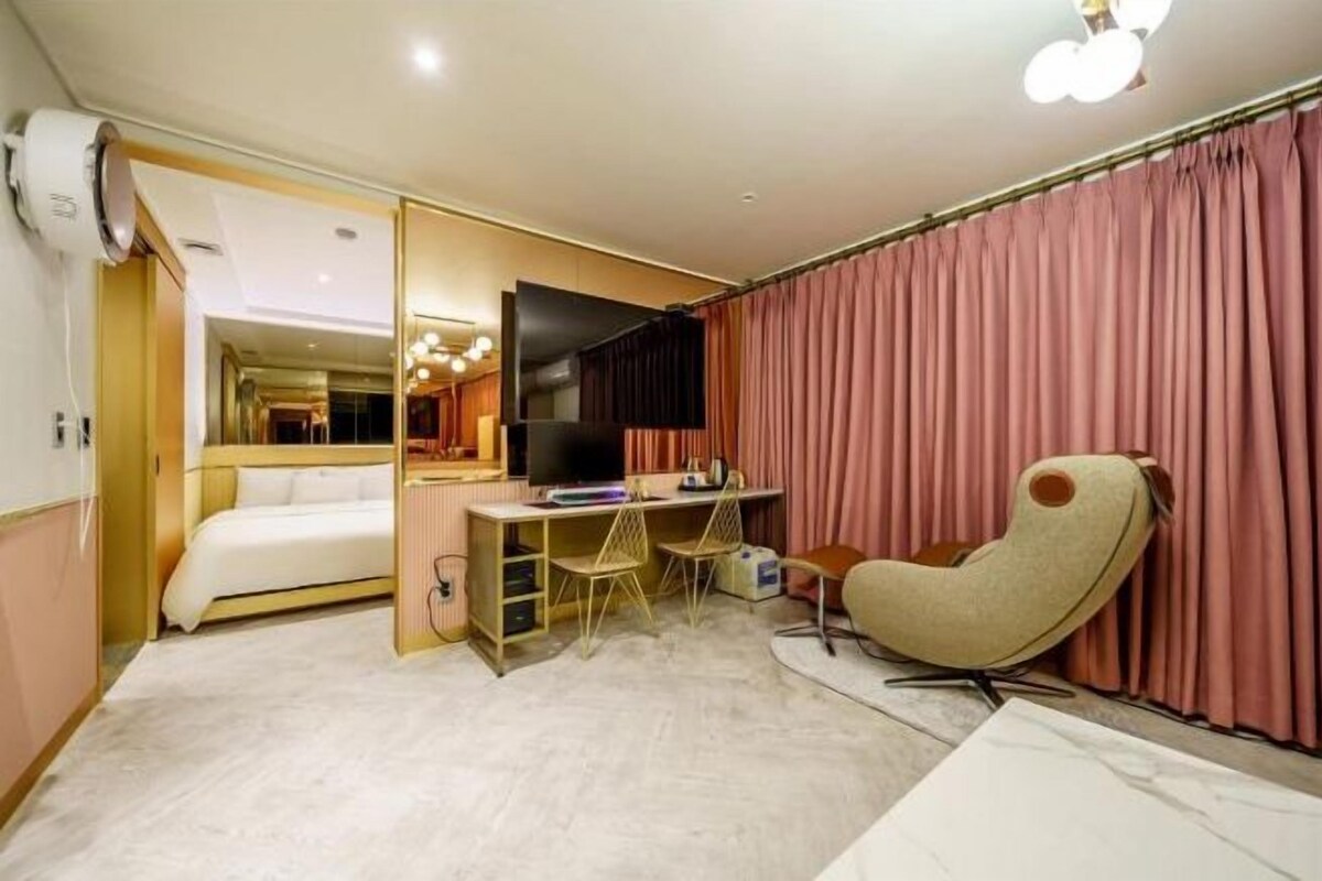 A compact hotel room with a bed, a desk with two chairs, a television, and a large mirror.