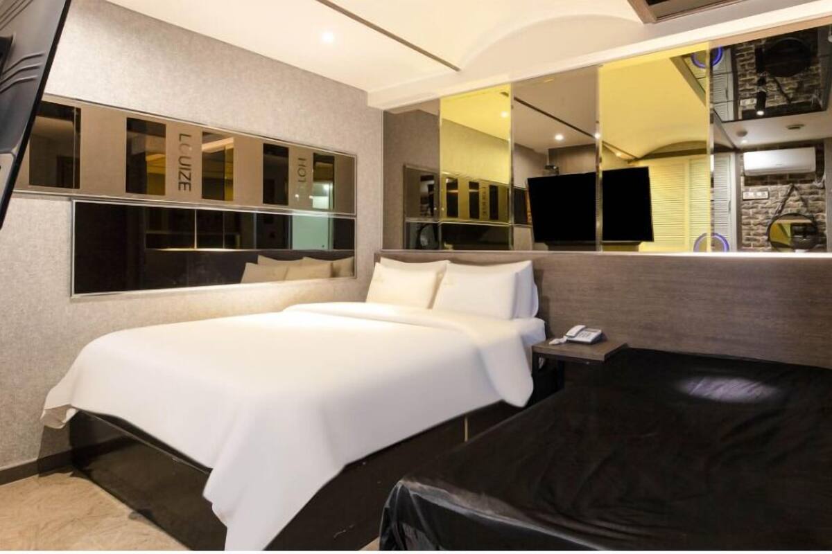 A modern hotel room with a large bed, a small desk, a mirror, and a television.