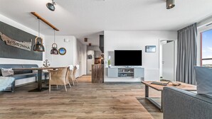 A modern living room with a sofa, dining table, and chairs, a TV, and a kitchen area in the background. - Pet friendly apartment in Kappeln (Kappeln)