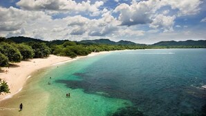 A beach with clear turquoise waters, a sandy shore, and lush green hills in the background.