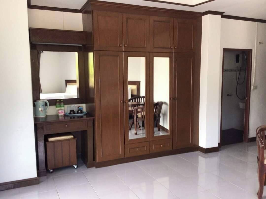 A room with a wooden cabinet with mirrored doors, a small table with a chair, and a tiled floor.