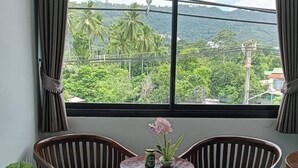 A room with two wooden chairs, a small table, and a window with a view of greenery and hills. - Samui Grand mansion (Koh Samui)