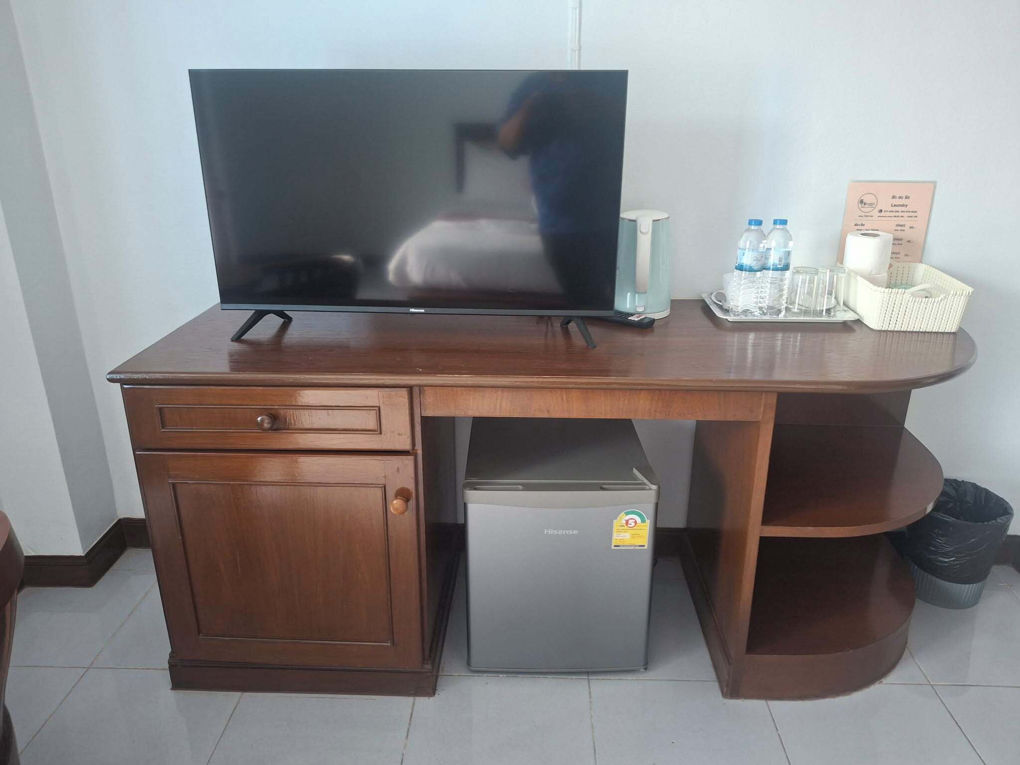 Un escritorio de madera con un televisor, un refrigerador pequeño y una cesta de artículos de aseo.