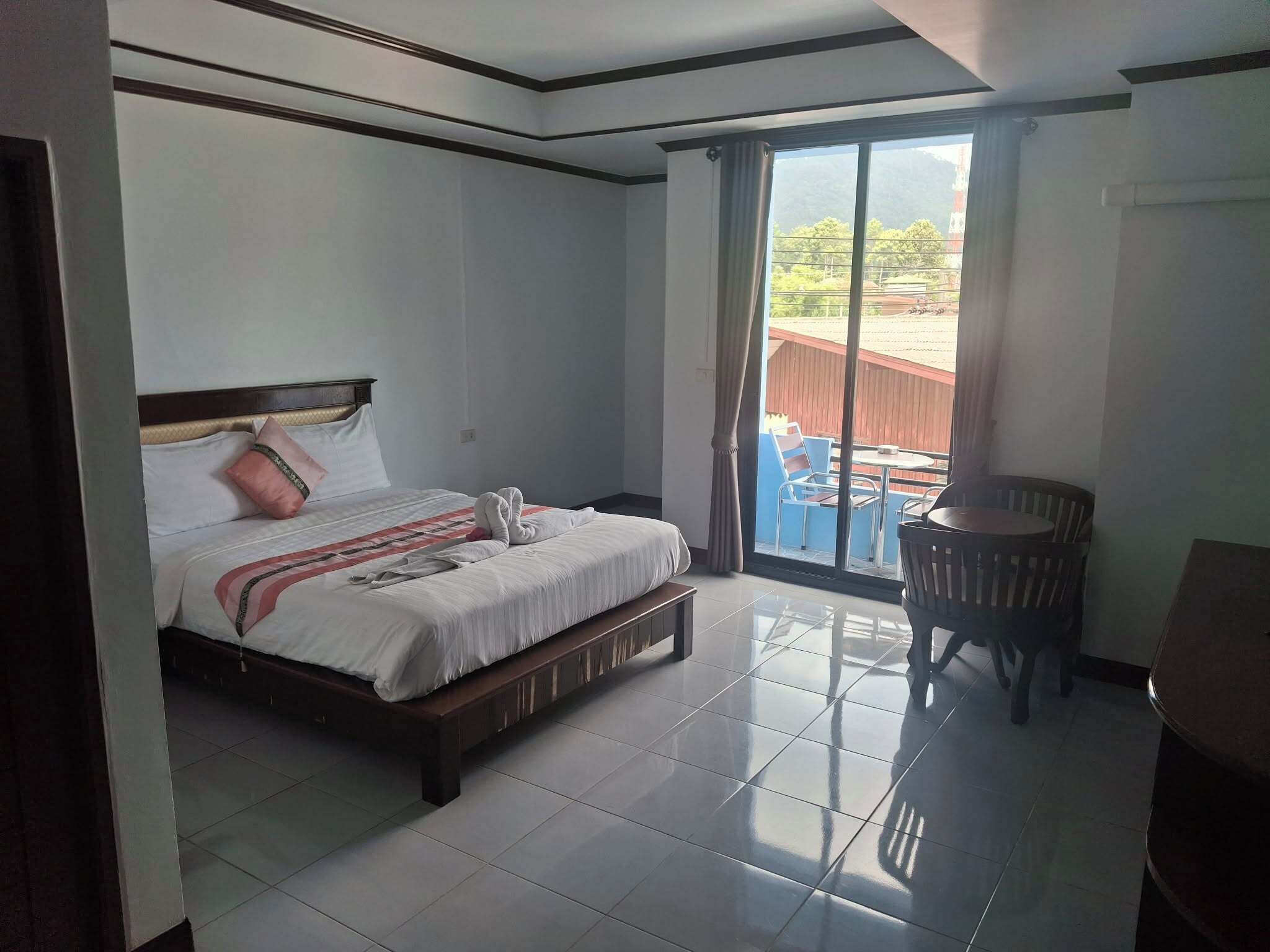 A hotel room with a bed, a small table, and a view of the outdoors.