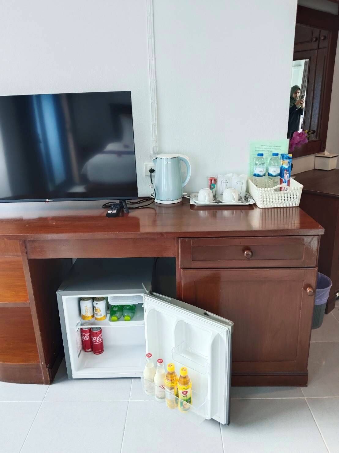 A kitchen area with a TV, a kettle, a refrigerator with beverages, and a basket of bottled water.