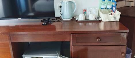 A kitchen area with a TV, a kettle, a refrigerator with beverages, and a basket of bottled water.