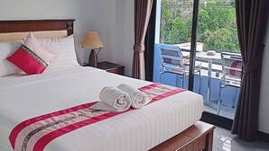 A hotel room with a large bed, a nightstand, a lamp, and a view of the outdoors through a sliding glass door. - Samui Grand mansion (Koh Samui)