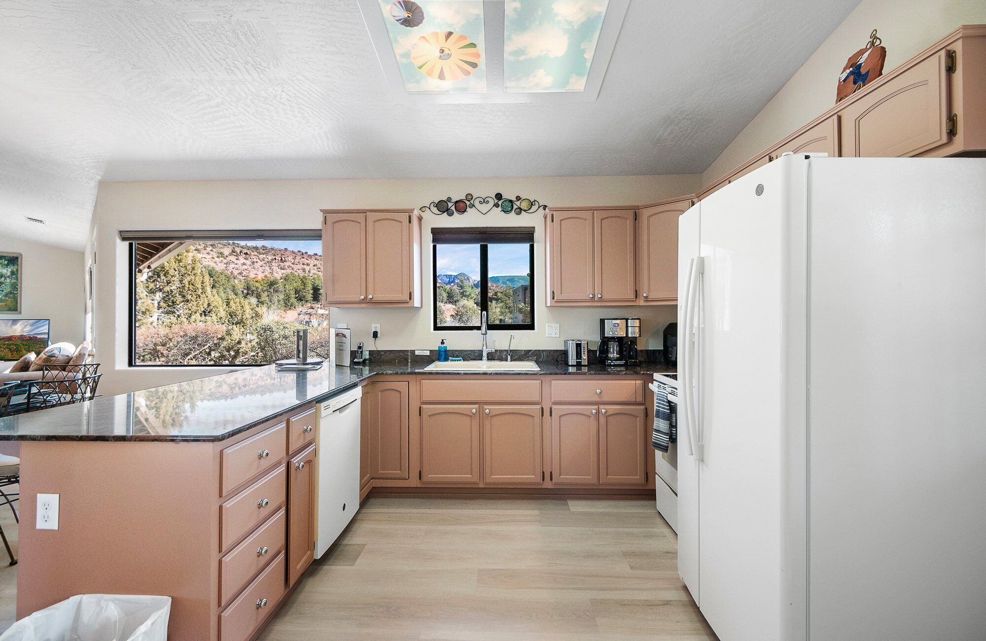 A kitchen with wooden cabinets, a white refrigerator, a sink, and a window overlooking a mountainous landscape.