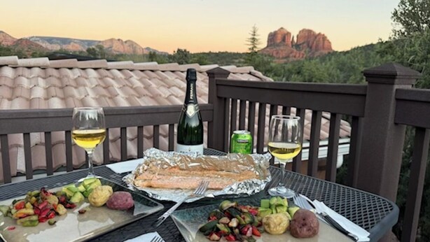 Ein Tisch mit Fisch, Gemüse und Getränken auf einem Balkon mit schöner Aussicht.