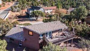 Ein modernes, zweistöckiges Haus mit Terrasse, umgeben von Bäumen und einer gebirgigen Landschaft.