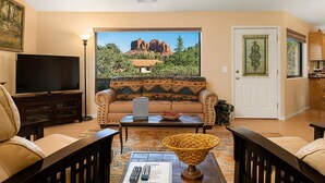 Ein Wohnzimmer mit einer Couch, einem Couchtisch und einem Fernseher. Eine Tür mit einer dekorativen Glasscheibe und ein Blick auf einen Berg durch ein Fenster.