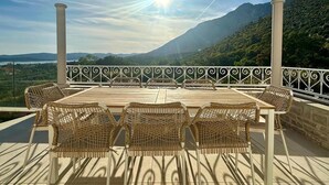 A terrace with a table and wicker chairs, overlooking a mountainous landscape.