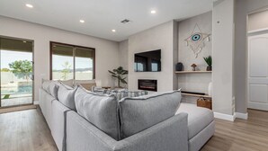 A modern living room with a grey sectional sofa, a flat-screen TV mounted on the wall, and a fireplace. - Modern South Mountain Heated Pool Trails Fire Pit (Phoenix)