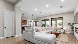 A spacious living room with a grey sectional sofa, a coffee table, and a large window providing natural light. - Modern South Mountain Heated Pool Trails Fire Pit (Phoenix)