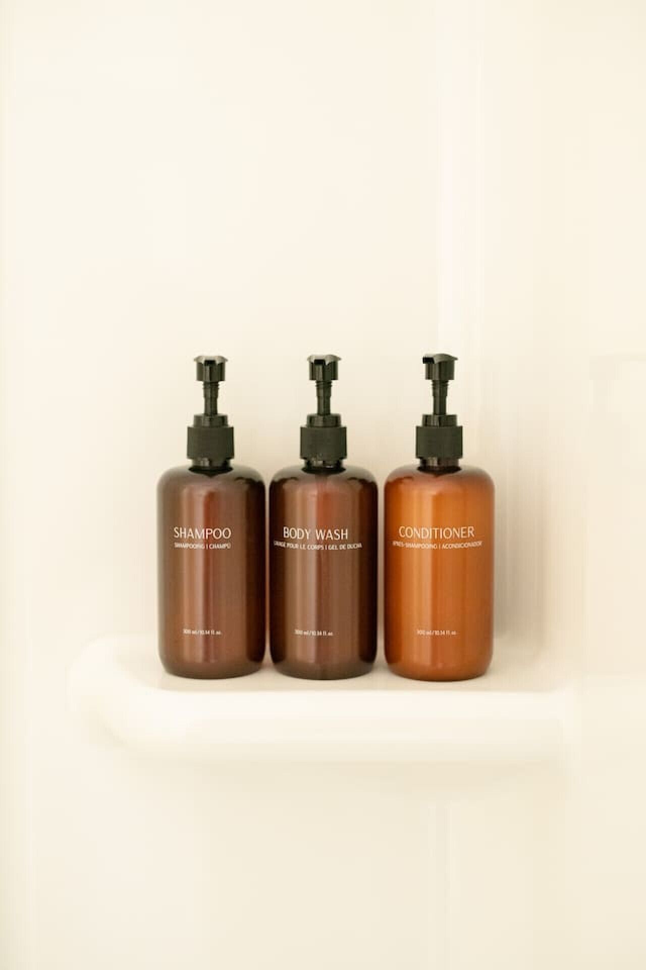 Tres botellas de champú, gel de baño y acondicionador sobre un estante blanco.