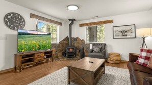 A living room with a stone fireplace, a large flat-screen TV, wooden furniture, and a cozy seating area. - Delightful 3-bedroom house in charming Flagstaff w/King Size Bed & Gas Log Stove (Flagstaff)