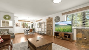 A spacious living room with a wooden coffee table, a television, and a stone fireplace. - Delightful 3-bedroom house in charming Flagstaff w/King Size Bed & Gas Log Stove (Flagstaff)