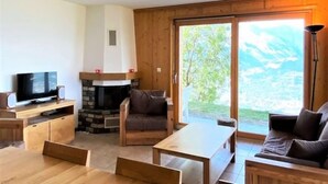 Een gezellige woonkamer met een open haard, een televisie en een groot raam met uitzicht op een schilderachtige omgeving.