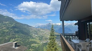 Un balcone con vista su un paesaggio montuoso, tra cui cime innevate e un villaggio sottostante.