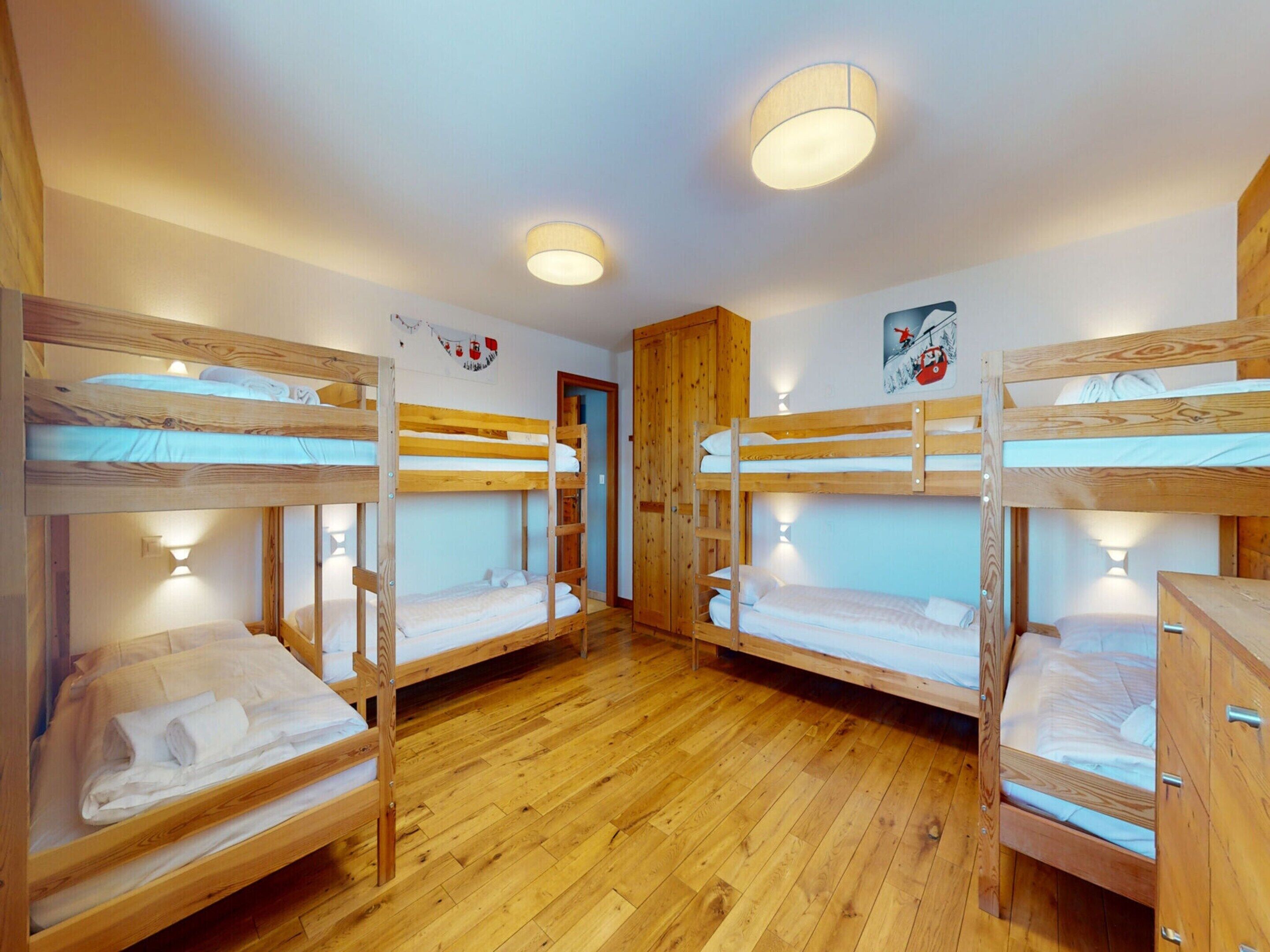 A room with four bunk beds, wooden flooring, and wall-mounted lights.