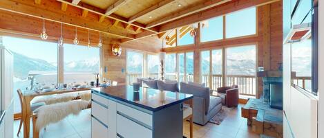 A spacious kitchen with a central island, large windows offering mountain views, and wooden beams on the ceiling.