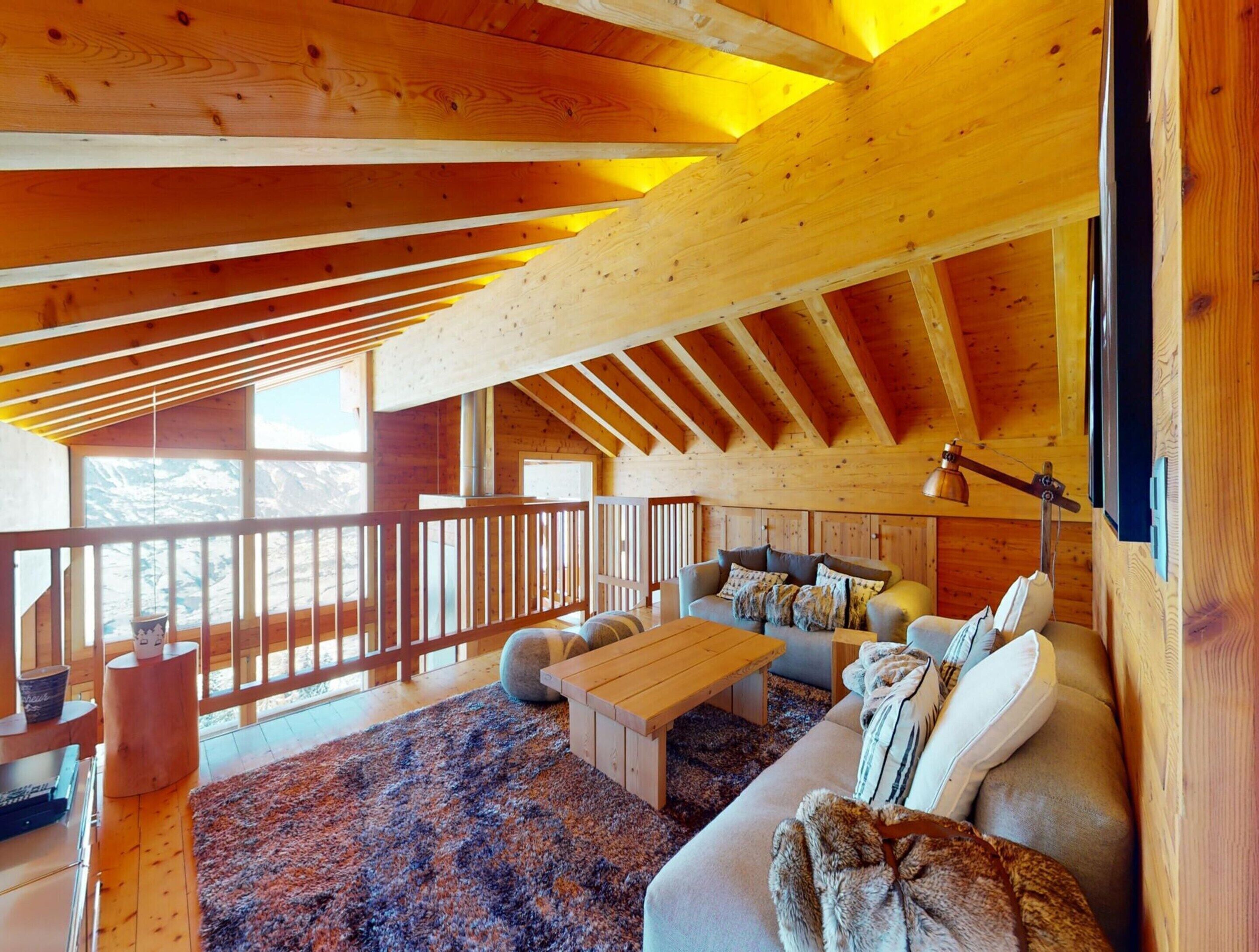 Interior acogedor de una cabaña de madera con techo alto, un ventanal grande, un sofá, una mesa de centro y una chimenea.