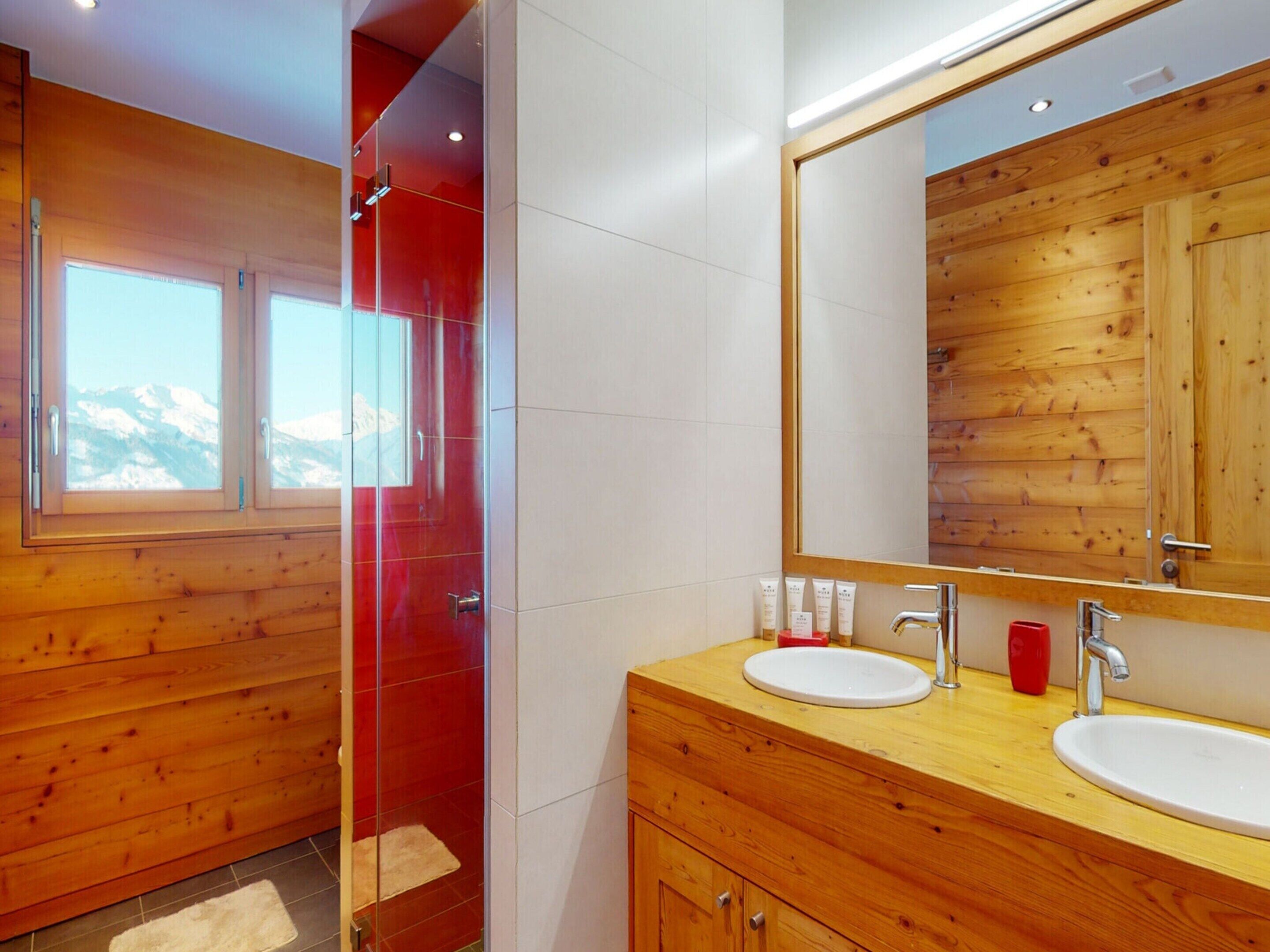 A modern bathroom with wooden paneling, two sinks, a large mirror, and a glass shower enclosure.