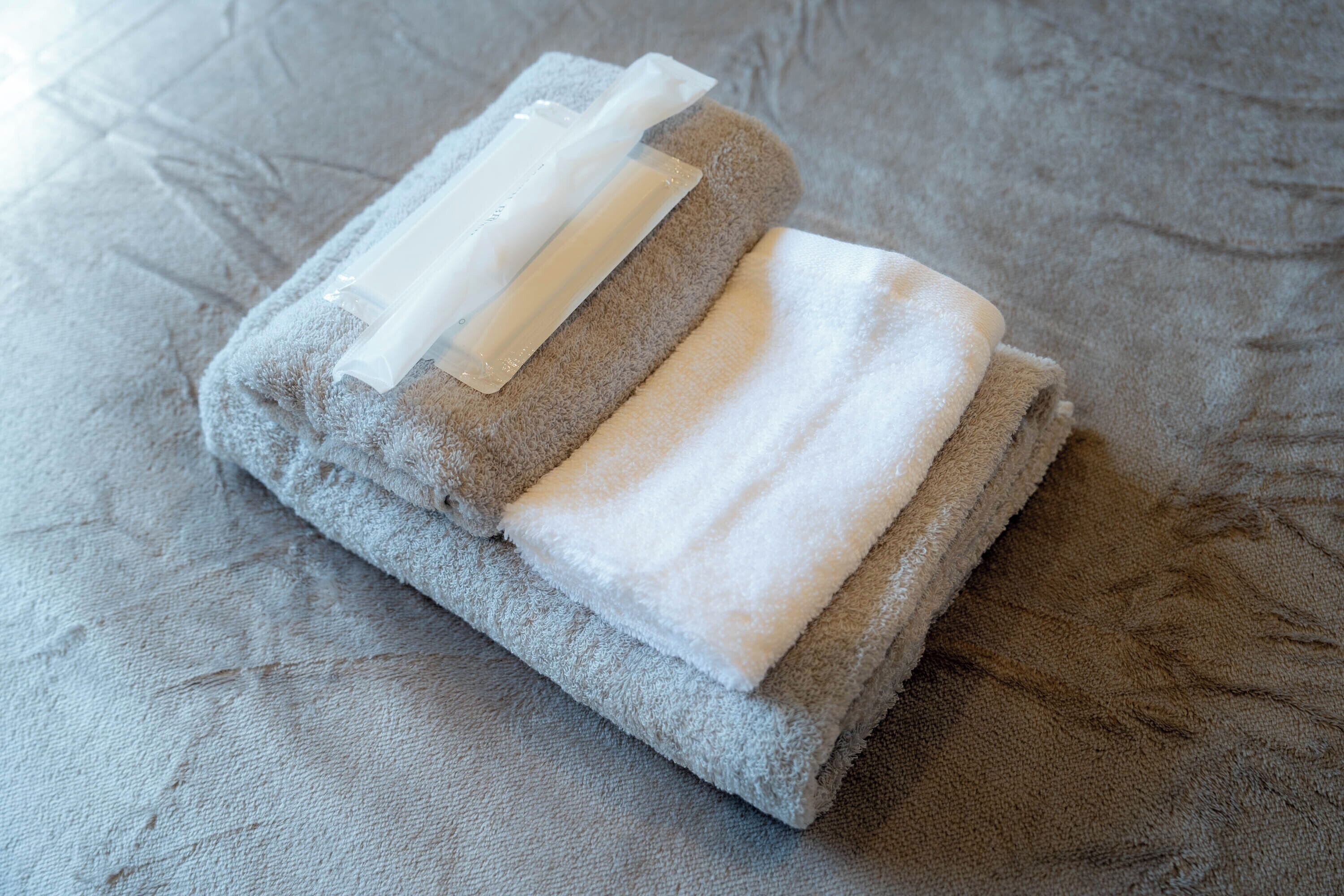 A neatly folded gray towel with a transparent plastic bag on a textured fabric surface.