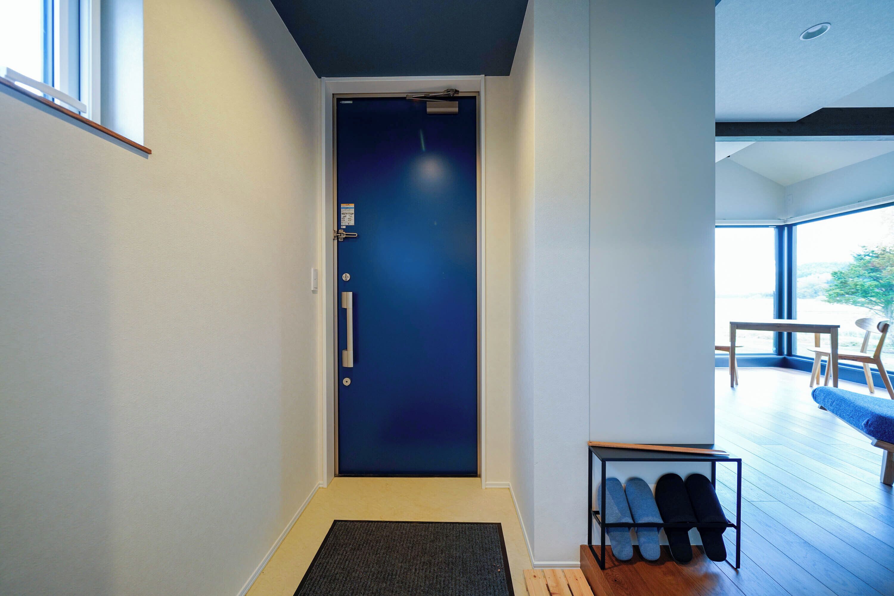 A hallway with a blue door, a small table with shoes, and a view of a balcony with outdoor seating.