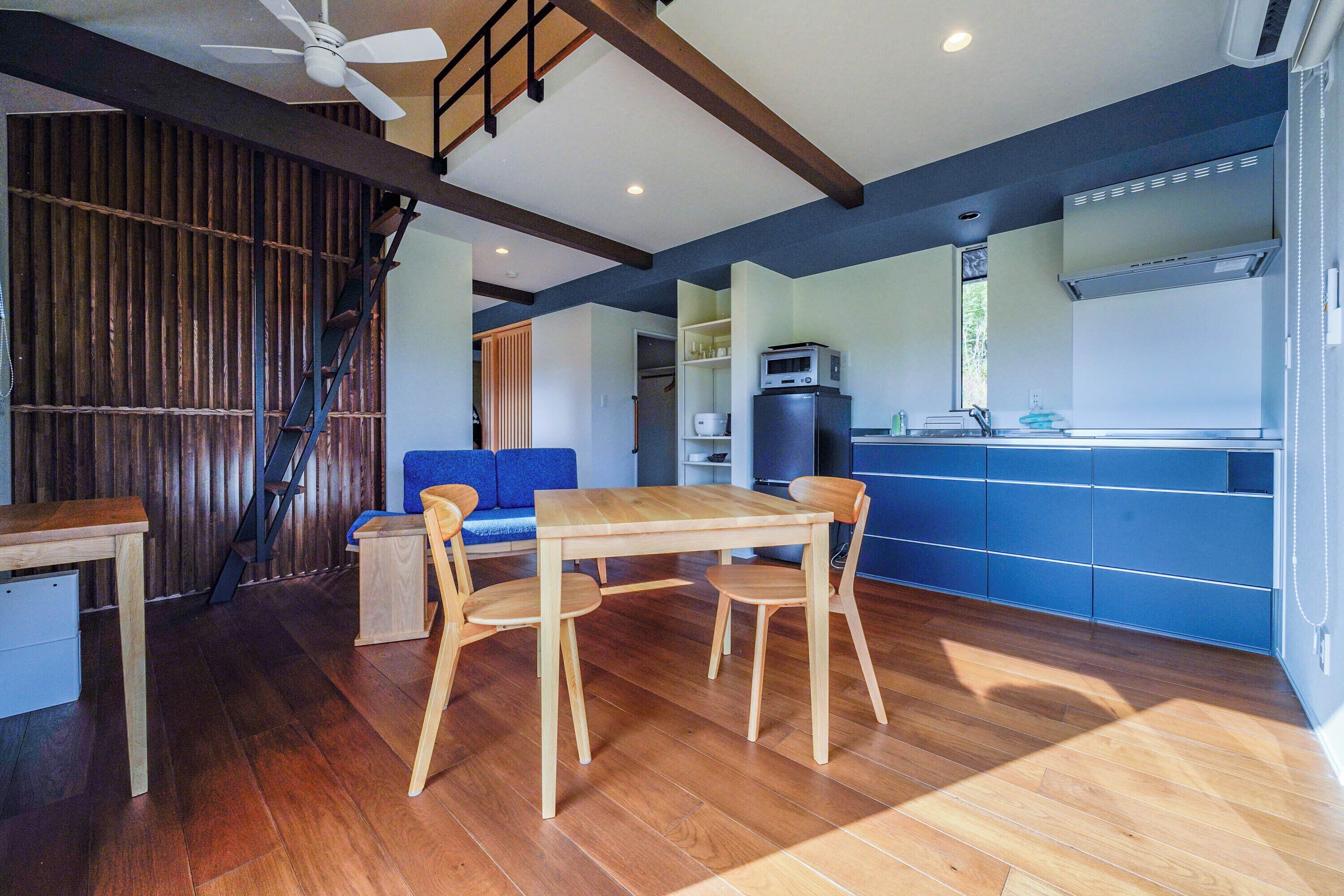 A modern kitchen with wooden flooring, a dining table with chairs, and a blue accent wall.