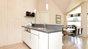 A modern kitchen with a built-in island, white cabinetry, and a large window providing natural light. - 5 Star Holiday Home in Grossenbrode (Grossenbrode)