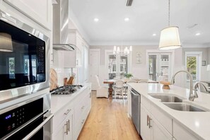 A modern kitchen with a built-in oven, a dining area with a table and chairs, and a large window. - Hola Beaches by Stay on 30a (Inlet Beach)